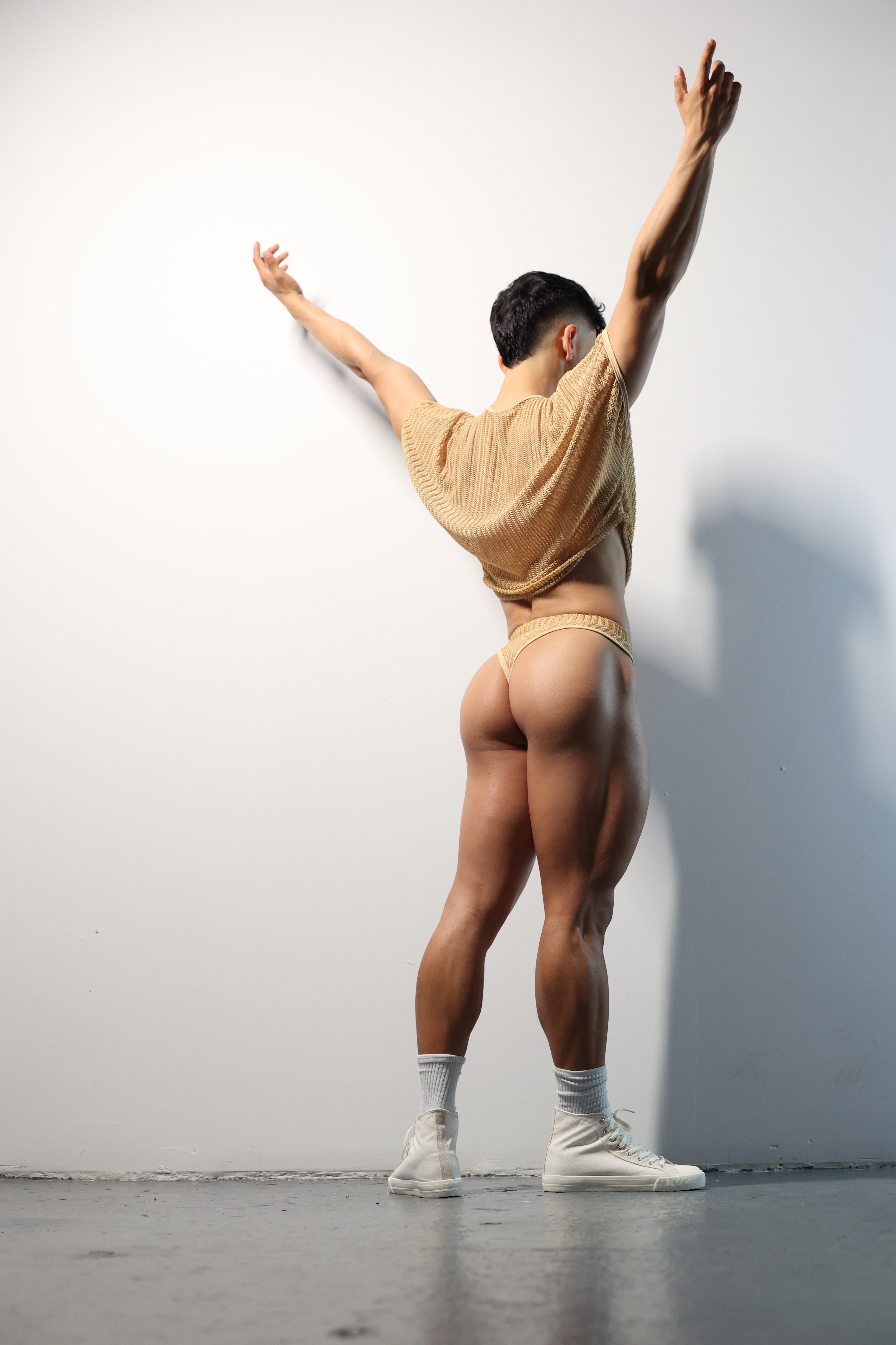 Fabian Divani modeling a netted natural crop top and swim brief set—handmade —posed in front of a white wall