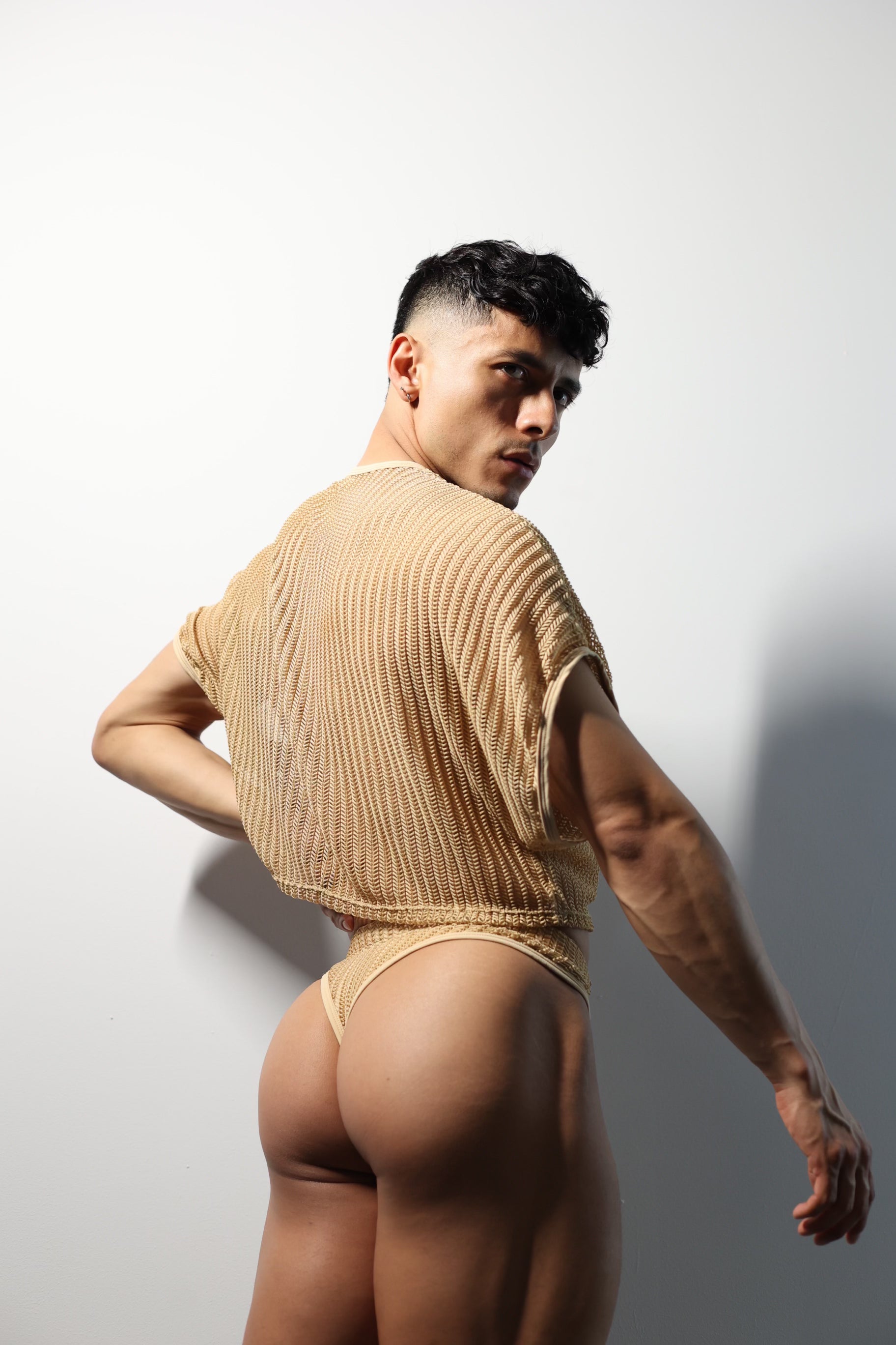 Fabian Divani modeling a netted natural crop top and swim brief set—handmade —posed in front of a white wall