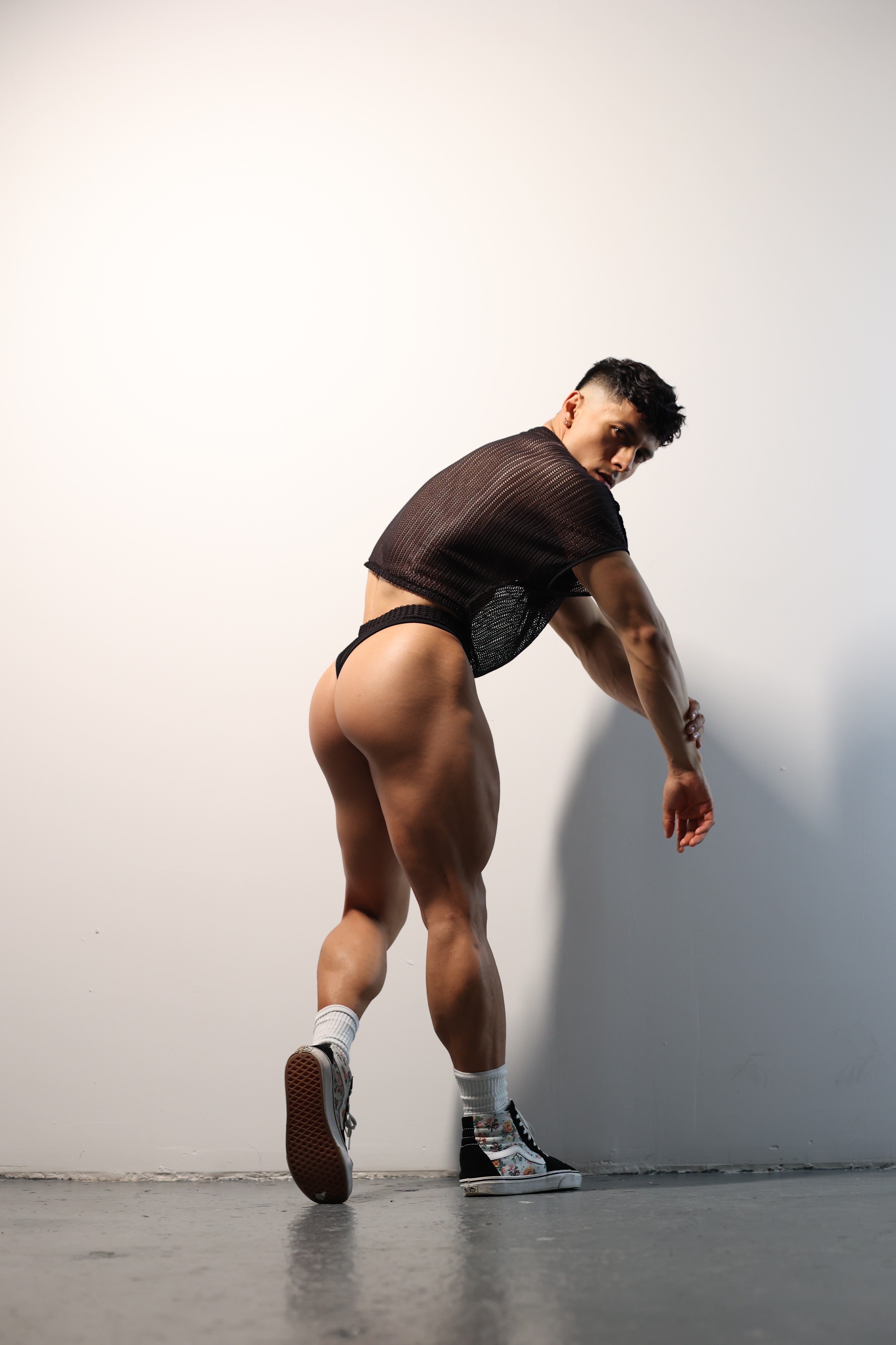 Fabian Divani modeling a sheer black mesh crop top and swim brief set—handmade by Fabi —posed in front of a white wall