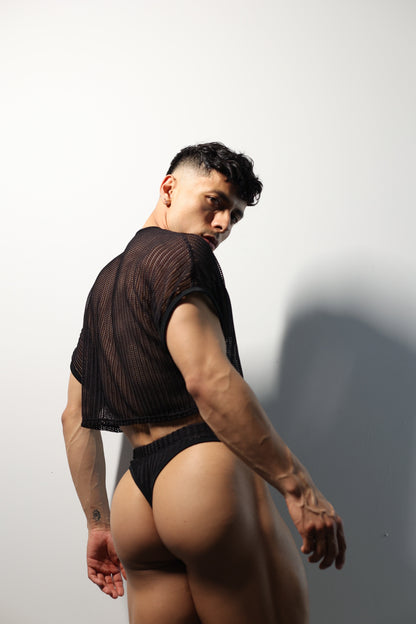 Fabian Divani modeling a sheer black mesh crop top and swim brief set—handmade by Fabi —posed in front of a white wall