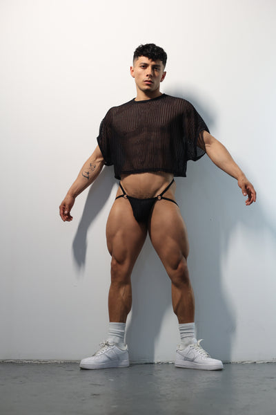 Fabian Divani modeling a sheer black mesh crop top and string jockstrap set—handmade men's underwear—posed in front of a white wall