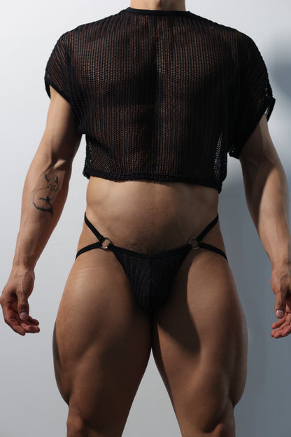 Fabian Divani modeling a sheer black mesh crop top and string jockstrap set—handmade men's underwear—posed in front of a white wall