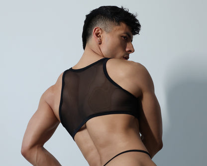 Fabian Divani modeling a sheer black ribbed mesh crop top and G-string underwear set—handmade by Fabi —posed in front of a white wall