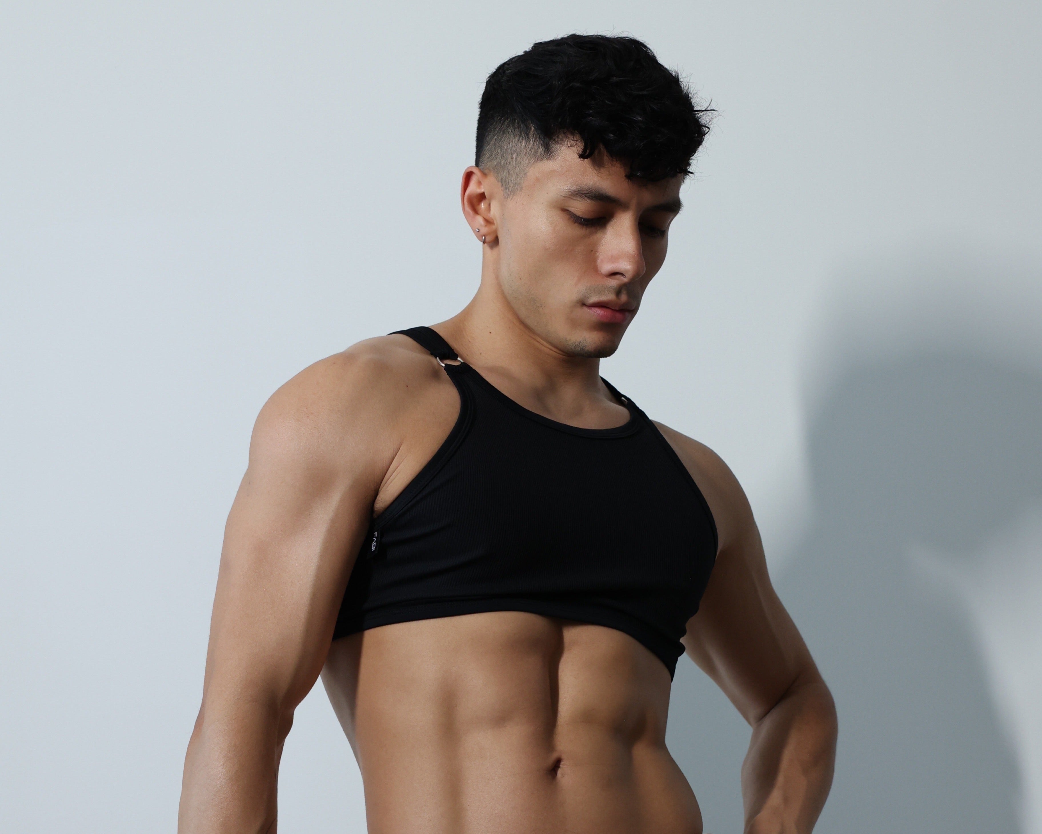 Fabian Divani modeling a sheer black ribbed mesh crop top and G-string underwear set—handmade by Fabi —posed in front of a white wall