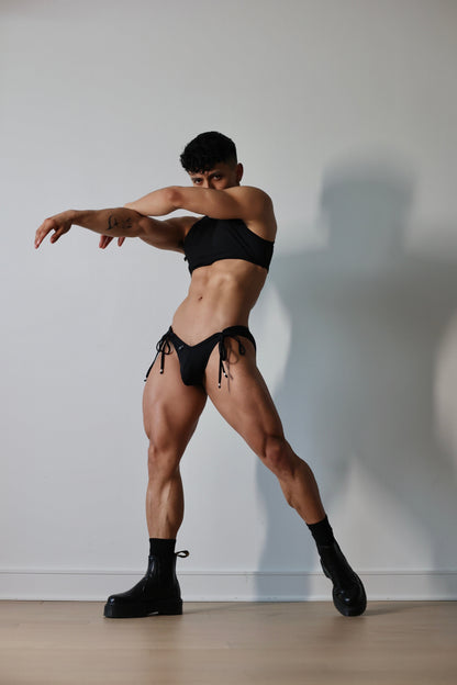 Fabian Divani modeling a sheer black ribbed mesh crop top and swim brief set—handmade by Fabi —posed in front of a white wall