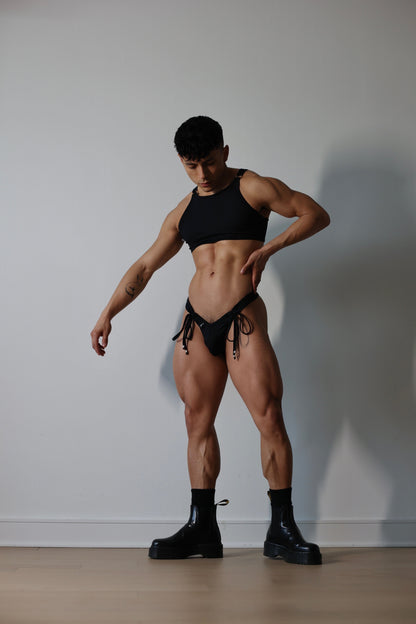 Fabian Divani modeling a sheer black ribbed mesh crop top and swim brief set—handmade by Fabi —posed in front of a white wall