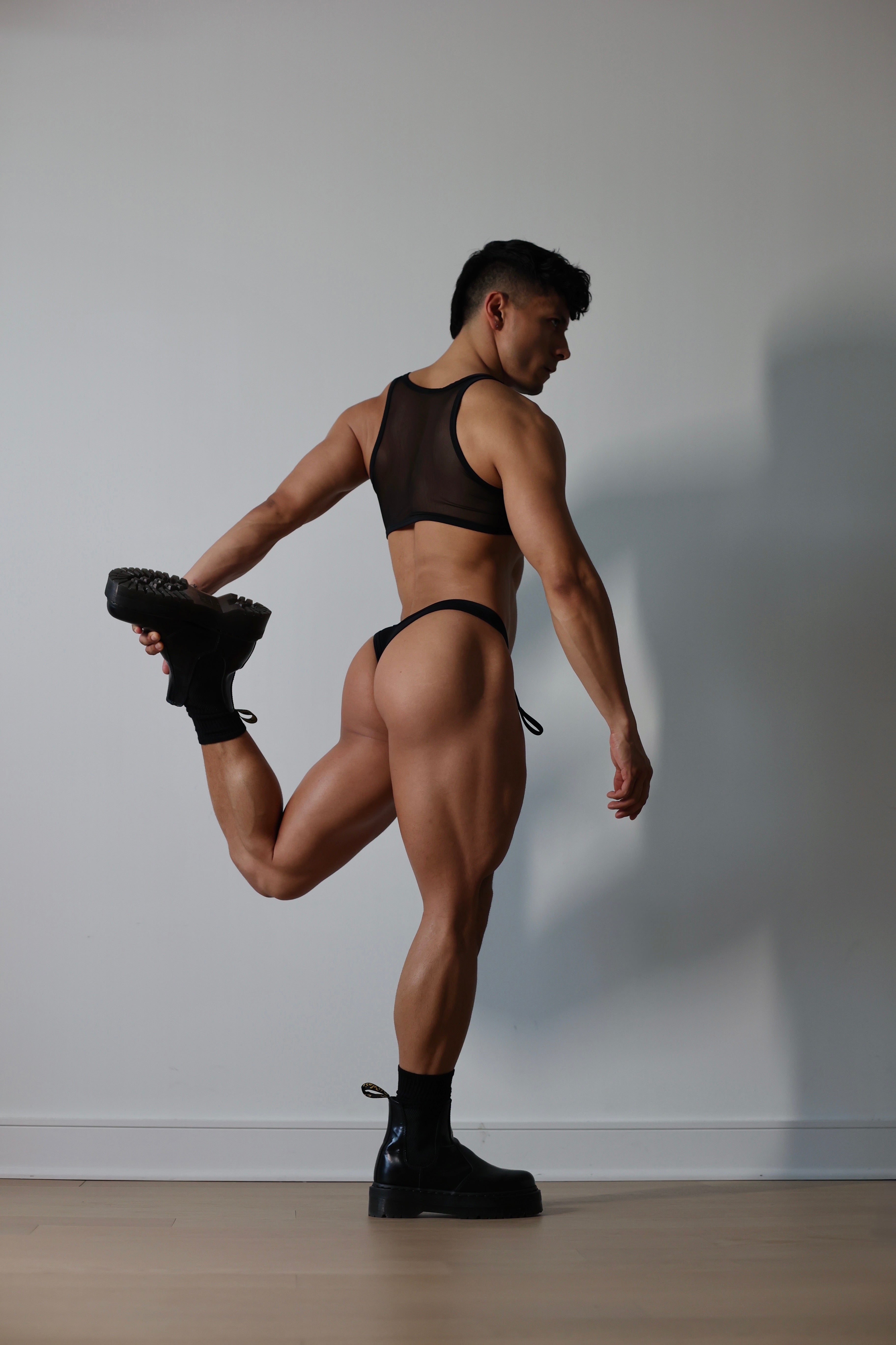 Fabian Divani modeling a sheer black ribbed mesh crop top and swim brief set—handmade by Fabi —posed in front of a white wall