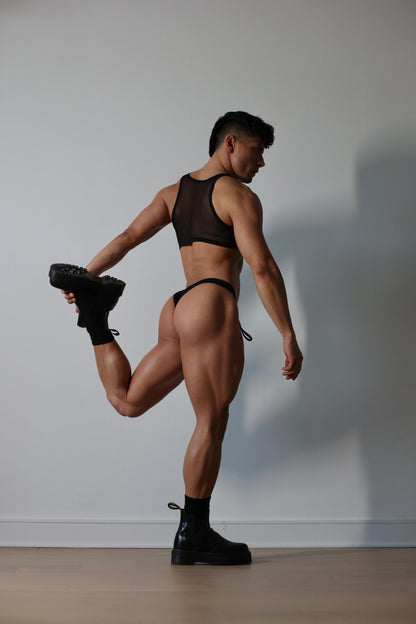 Fabian Divani modeling a sheer black ribbed mesh crop top and swim brief set—handmade by Fabi —posed in front of a white wall