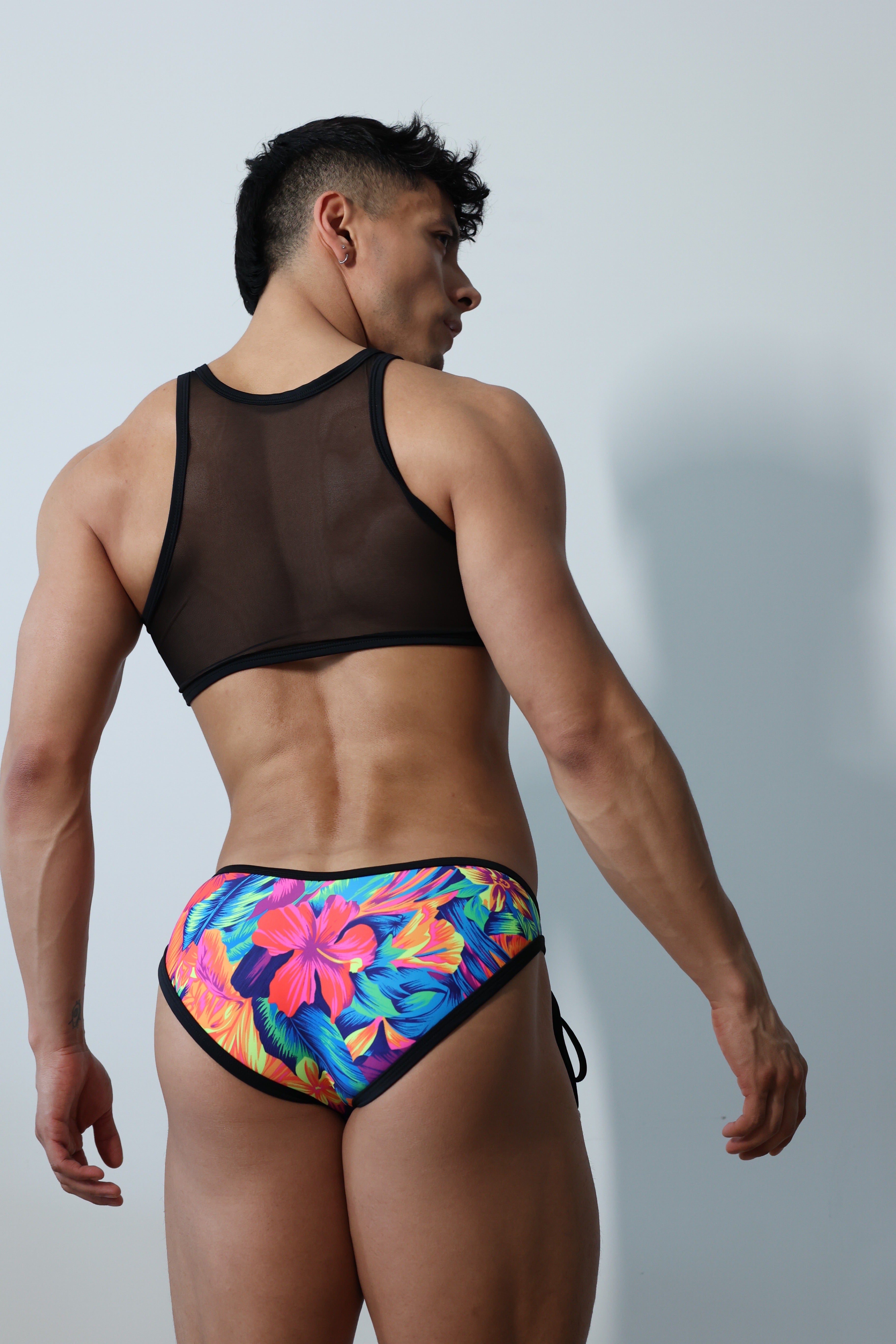 Fabian Divani modeling a sheer floral mesh crop top and swim brief set—handmade by Fabi —posed in front of a white wall