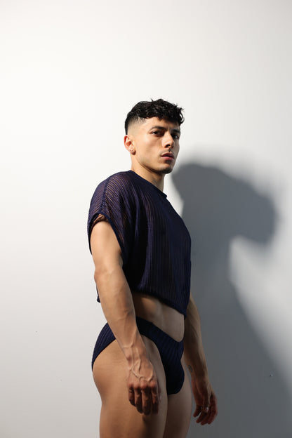 Fabian Divani modeling a sheer midnight blue mesh crop top and swim brief set—handmade men's swimwear—posed in front of a white wall