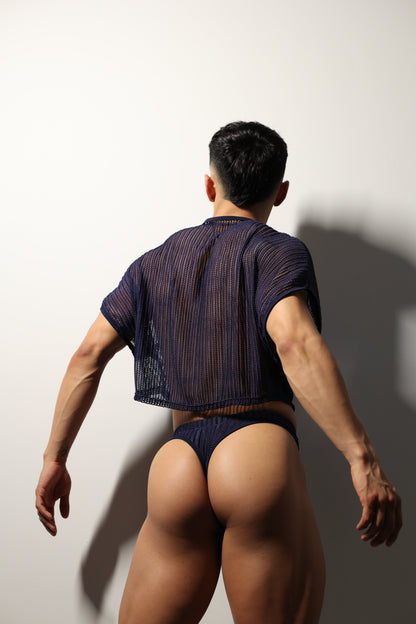 Fabian Divani modeling a sheer midnight blue mesh crop top and swim brief set—handmade men's swimwear—posed in front of a white wall