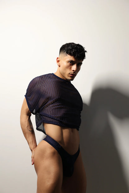 Fabian Divani modeling a sheer midnight blue mesh crop top and swim brief set—handmade men's swimwear—posed in front of a white wall