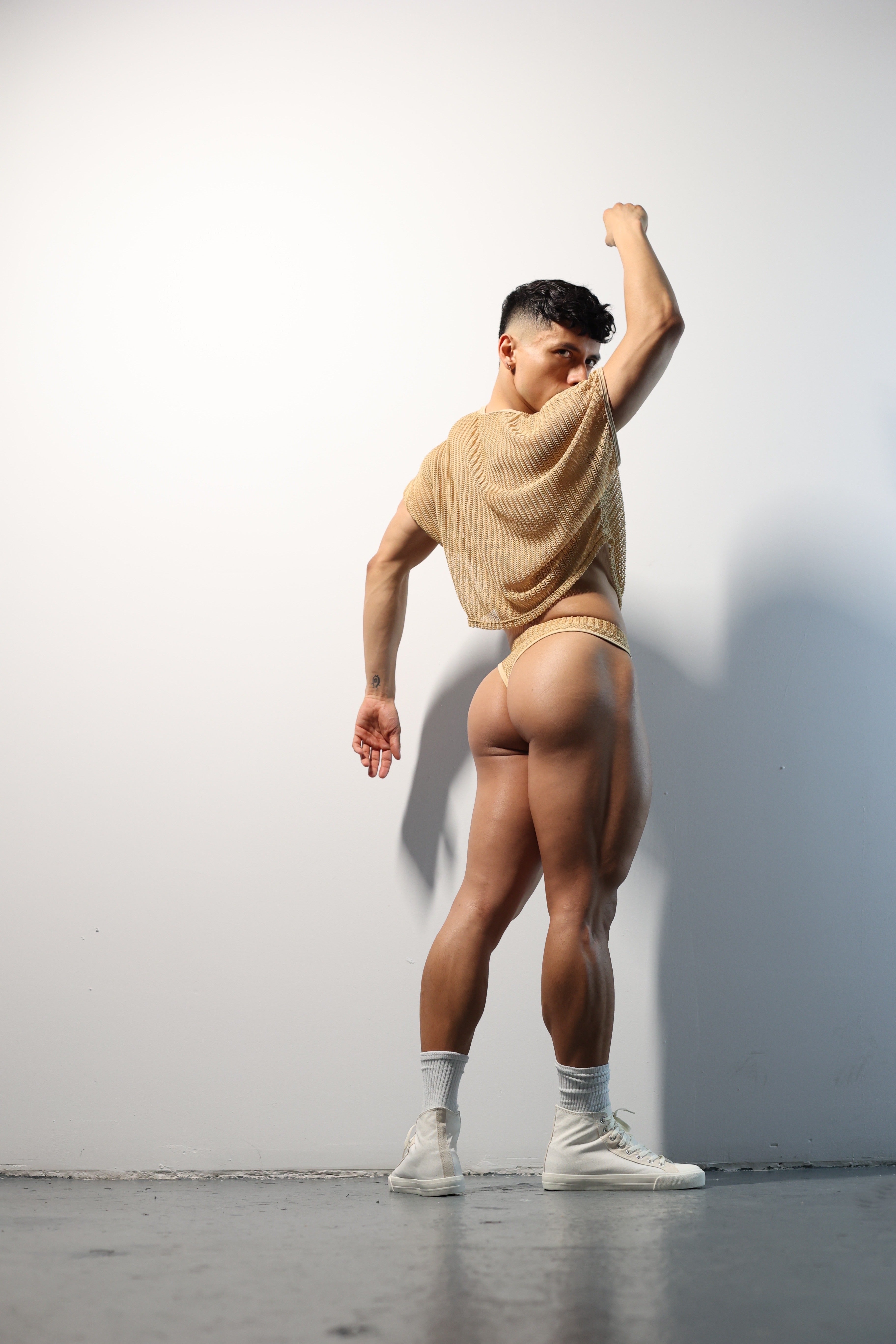 Fabian Divani modeling a netted natural crop top and swim brief set—handmade —posed in front of a white wall