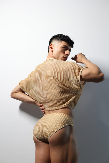 Fabian Divani modeling a sheer natural mesh crop top and swim brief set—handmade men's swimwear—posed in front of a white wall