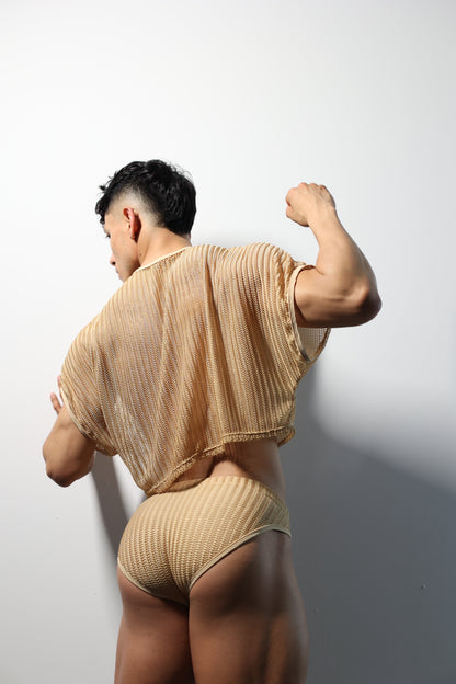 Fabian Divani modeling a sheer natural mesh crop top and swim brief set—handmade men's swimwear—posed in front of a white wall