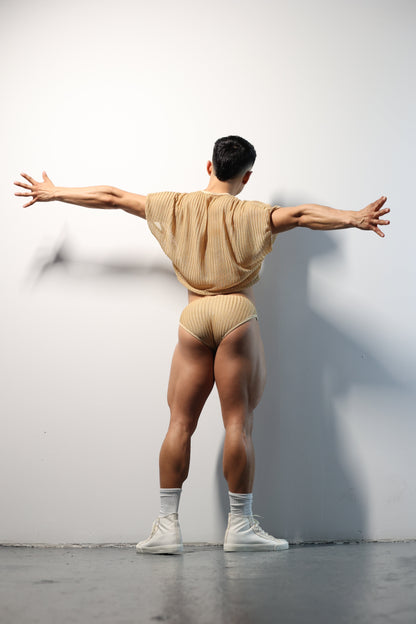 Fabian Divani modeling a sheer natural mesh crop top and swim brief set—handmade men's swimwear—posed in front of a white wall
