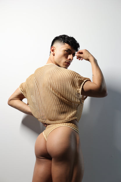 Fabian Divani modeling a sheer natural mesh crop top and swim brief set—handmade men's swimwear—posed in front of a white wall
