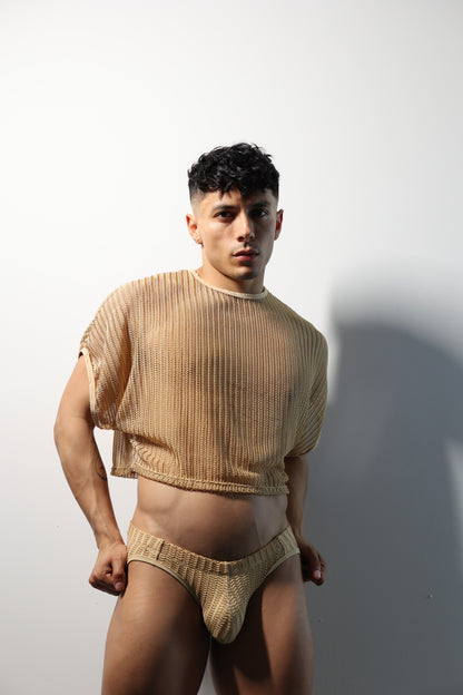 Fabian Divani modeling a sheer natural mesh crop top and swim brief set—handmade men's swimwear—posed in front of a white wall