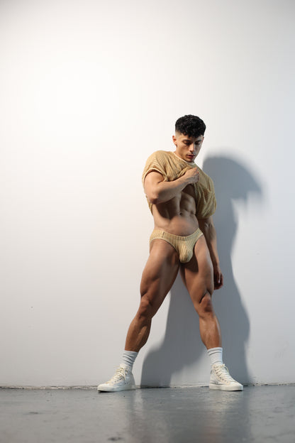 Fabian Divani modeling a sheer natural mesh crop top and swim brief set—handmade men's swimwear—posed in front of a white wall