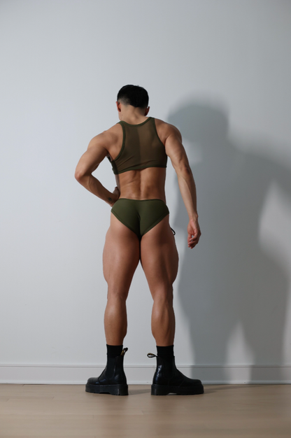 Fabian Divani modeling a sheer olive crop top and swim brief set—handmade men's swimwear—posed in front of a white wall