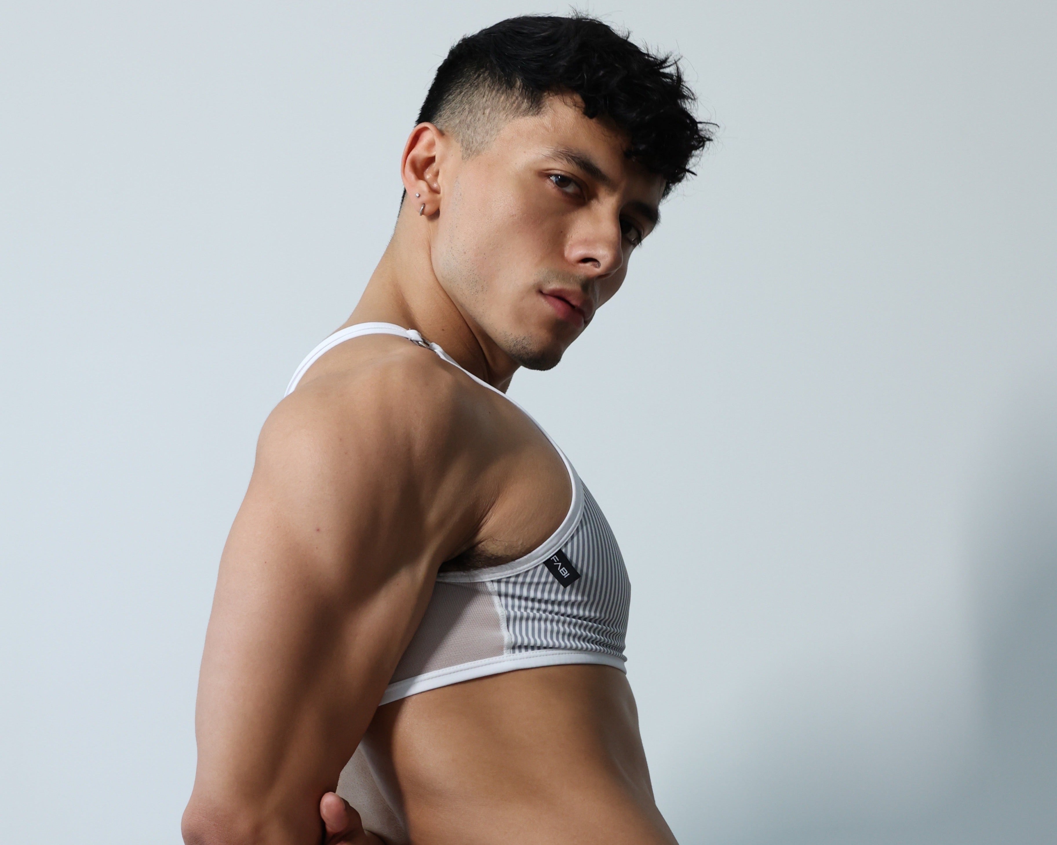 Fabian Divani modeling a sheer  pinstripe mesh crop top and G-string underwear set— handmade men's underwear — posed in front of a white wall