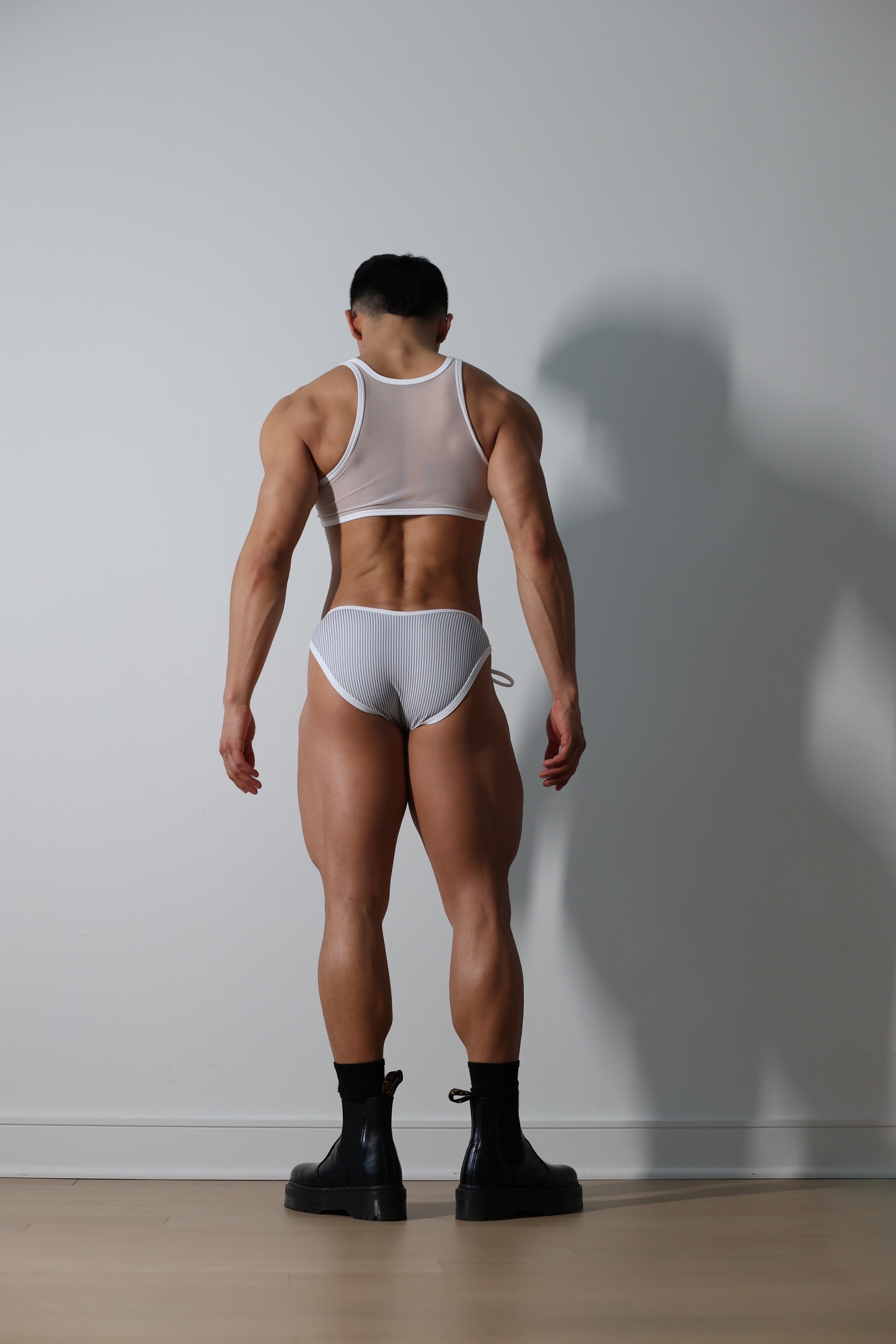 Fabian Divani modeling a sheer Pinstripe mesh crop top and swim brief set—handmade men's swimwear—posed in front of a white wall