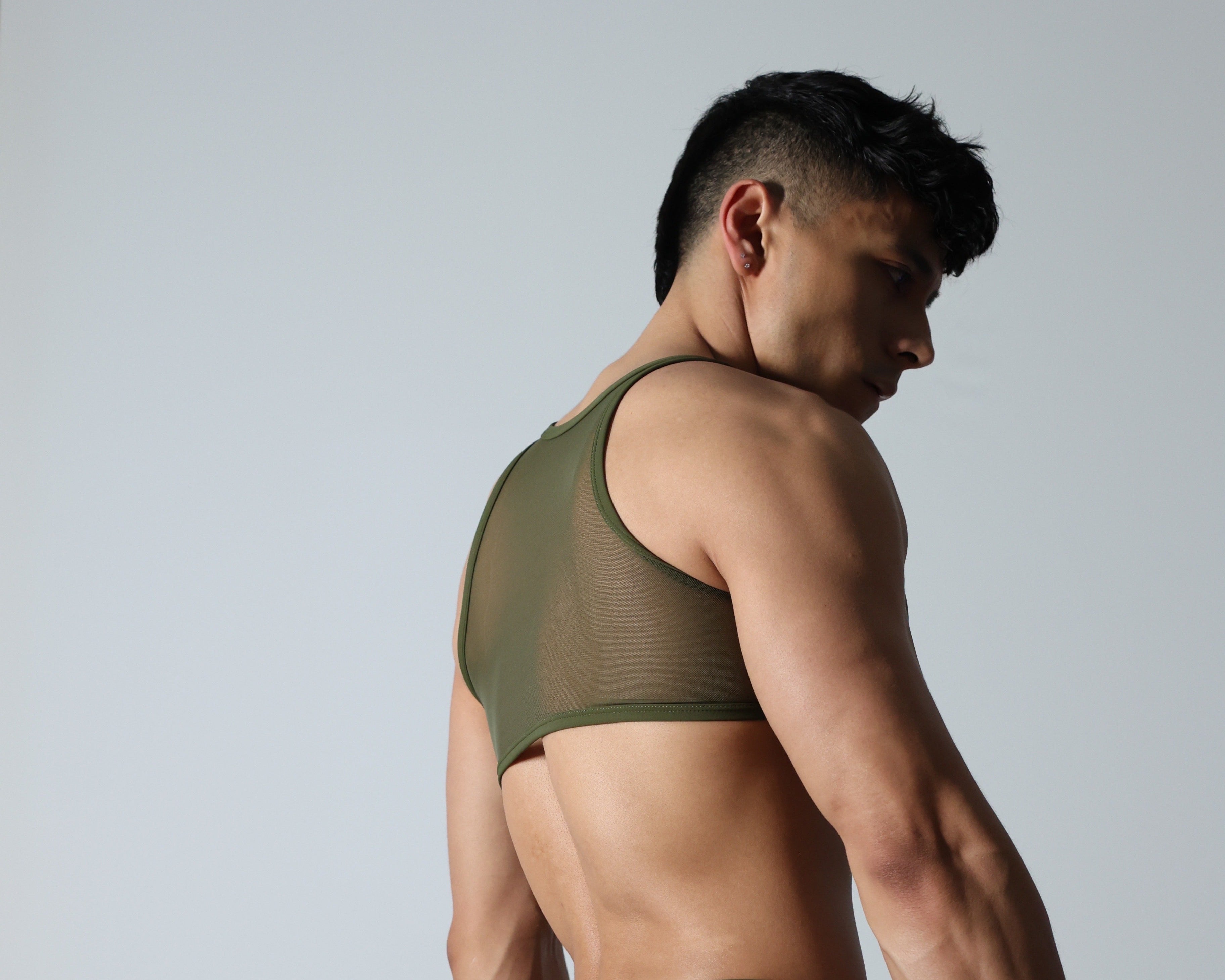 Fabian Divani modeling a sheer olive green mesh crop top —handmade by Fabi —posed in front of a white wall